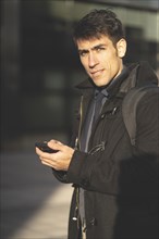 Portrait of businessman walking in the street texting with his phone