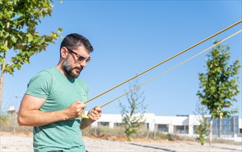 Bearded man with sunglasses seen in profile training his biceps with an elastic fitness band in an outdoor gym