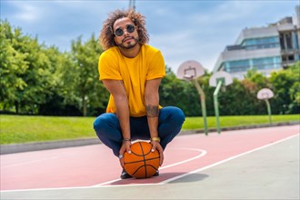 Portrait of an afro-haired man in a yellow t-shirt with a basketball ball. Portrait on a basketball court in the city