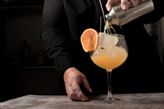 Waitress dressed in black serving an orange cocktail with ice and orange slice with a cocktail shaker