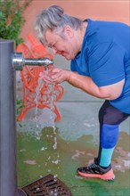 Older white-haired woman in sportswear drinking water from a fountain after workout