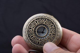 Retro style pocket watch in hand on black background