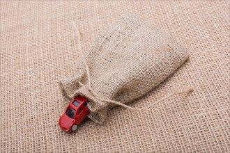 Red toy car coming out of a linen sack on a linen canvas