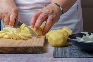 Close-up of a woman's hands in a white apron cutting potatoes with a knife