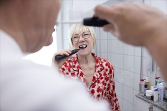 Elderly couple brush their teeth together in the bathroom