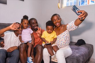Black African ethnicity family with their children on the sofa at home taking a selfie with their phone