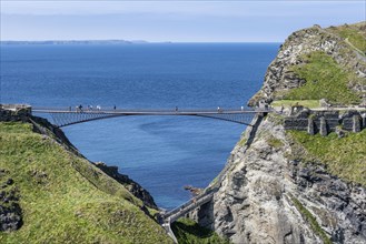 Tourists walk across the new footbridge to the peninsula with the castle ruins of Tintagel Castle