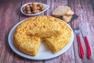 Typical spanish potato omelette freshly made on a wooden table with cutlery