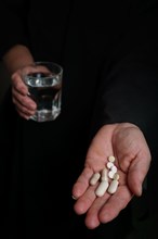 Person in darkness with pills in one hand and a glass of water in the other black background and copy space