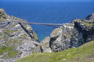 Tourists walk across the new footbridge to the peninsula with the castle ruins of Tintagel Castle