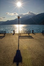 Bench and Street Lamp with Sunbeam on the Waterfront with Mountain in Ascona