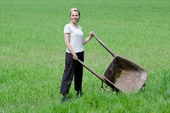 Woman with a Wheelbarrow on the Green Field with Grass