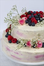 Summery fresh two tier wedding cake decorated with berries and flowers festive cream cake on light background