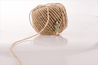 Woman figure beside a linen spool of thread on a white background