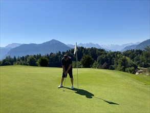 Golfer on Putting Green with Mountain View in a Sunny Summer Day in Burgenstock