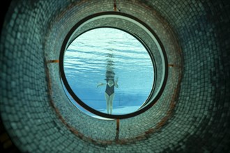 Woman Standing in the Ship Porthole in Underwater in Swimming Pool in a Sunny Day in Switzerland