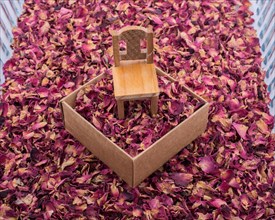Toy chair on a box filled with dry rose petals
