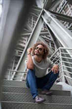 Young man with afro hair wearing sunglasses on the stairs in the city sitting