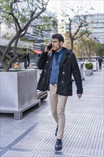 A handsome businessman having a conversation on his smartphone while walking in the street near his office