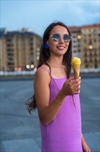 Portrait of young brunette woman smiling eating a mango ice cream next to the beach on summer vacation