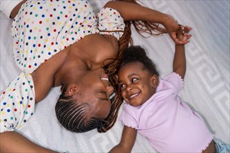 Black African ethnicity family mother with daughter in bedroom on bed smiling