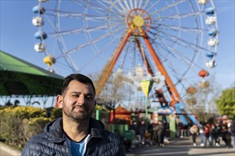 Portrait of latino man in an amusement park posing happy with the ferris wheel in the background
