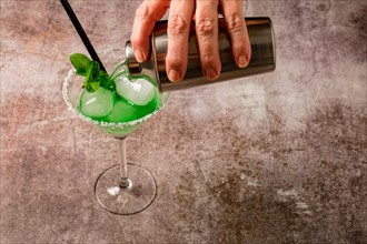 Hand of a woman serving a mint cocktail with ice straw and mint leaves with a cocktail shaker