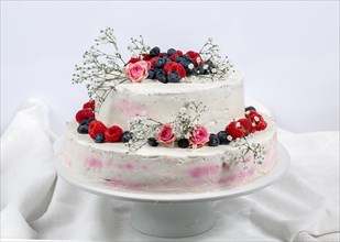 A two tier wedding cake decorated with berries and flowers festive cream cake on a light background