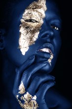 Fashion portrait of a blue-skinned girl with gold make-up.Beauty face. Picture taken in the studio on a black background