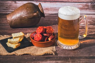 Mug of fresh beer with foam and clay pot with bread and chorizo sausage