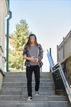 Long-haired young man in plaid shirt and jeans comes down stairs