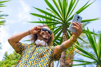 Afro-haired man on summer vacation next to some palm trees next to the beach taking a selfie. Travel and tourism concept