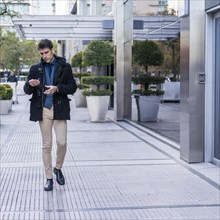 A serious businessman reading a message on his smartphone while walking in the street near his office