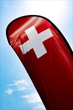 Swiss Banner Flag Against Blue Sky and Sunlight in Switzerland