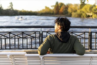 Back view of a man sitting on a bench at sunset contemplating the river