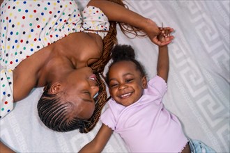 Black African ethnicity family mother with daughter in bedroom on bed smiling