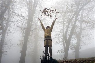 Woman Throwing Autumn Leaves Up in the Air in a Foggy Forest in Switzerland