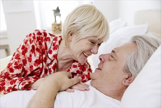 Elderly couple lying together in bed in bedroom laughing at each other in love