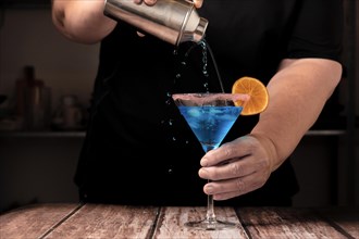 Waiter dressed in black serving a blue cocktail with sugar in the glass and a slice of orange