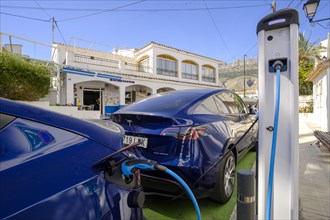 Two Tesla electric vehicles charging at a charging station in the village of Altea La Vella
