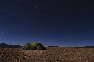 Stars in cloudless sky at night and dome tent with touring bicycle of adventurous hiker on high plateau of the Altiplano