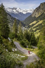 Mountain biker riding ascending winding road with hairpin bends in the Montafon region in autumn