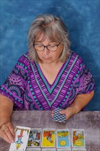 Older woman with white hair and glasses casting tarot cards