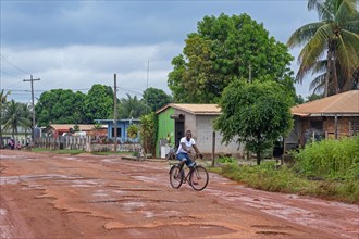 Local cyclist riding along muddy dirt road in the village Lethem during the rainy season