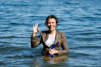 Elegant and happy wet woman in the water with a diving mask and a suit and showing ok signal