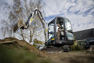 A construction worker sits in a mini-excavator at a building site. Berlin