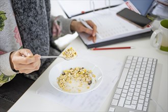 Symbolic photo on the subject of eating at the workplace. A woman eats a muesli at her desk. Lunch break at the workplace