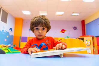 Portrait of a boy sitting at a table reading a story book looking at the camera