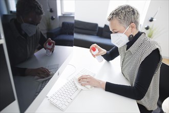 Hygiene at the workplace. A woman disinfects the keyboard at her workplace with disinfectant spray. Berlin