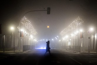 A woman walks along a street decorated with Christmas lights in the fog in Niesky